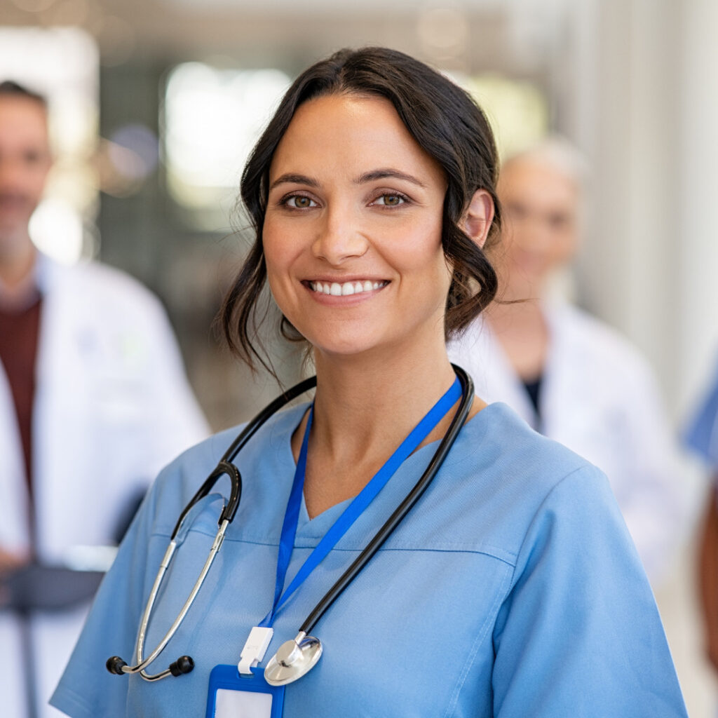 A nurse wearing a stethoscope and blue scrubs smiling