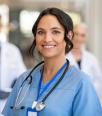 A nurse wearing a stethoscope and blue scrubs smiling