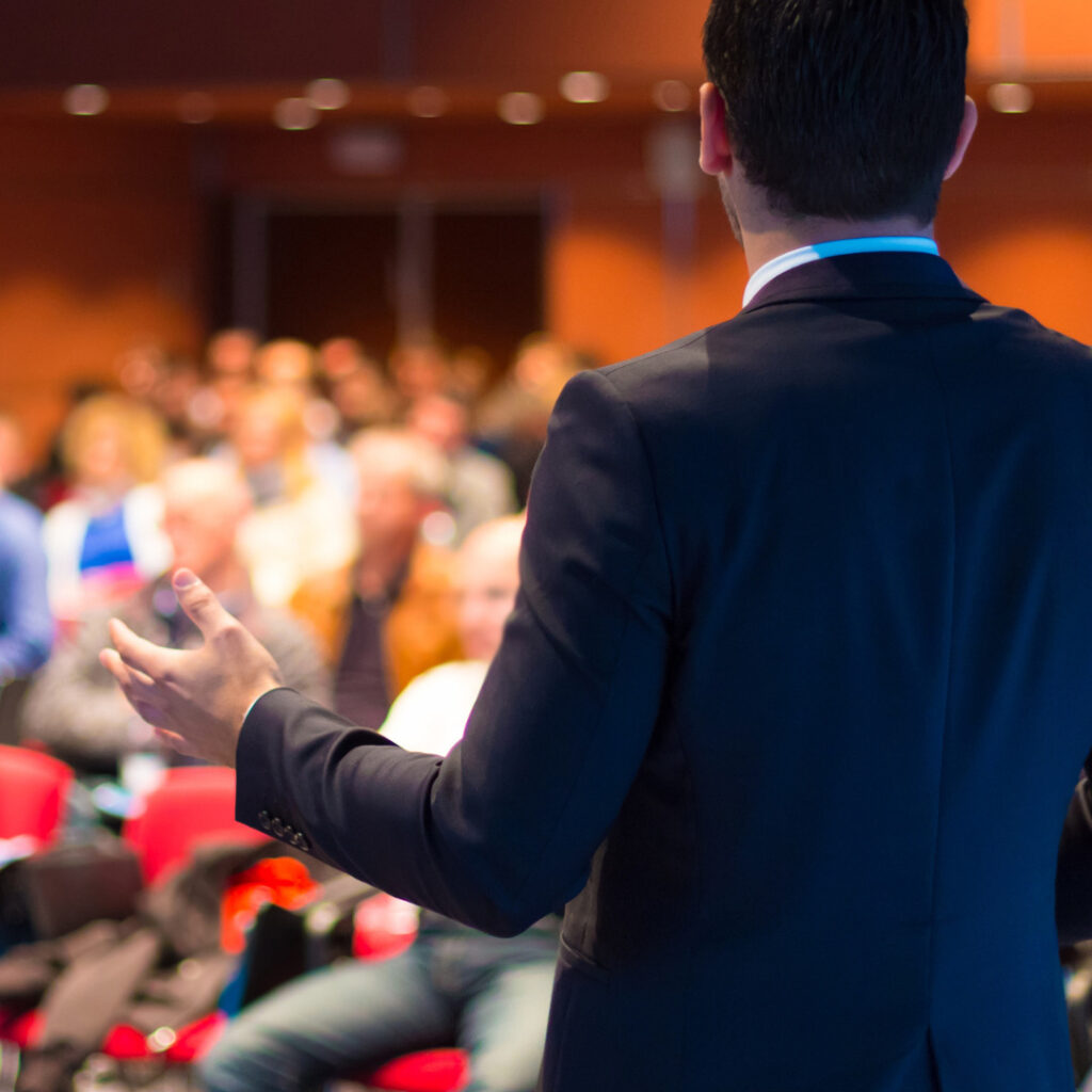 A person speaks to a crowd at a conference