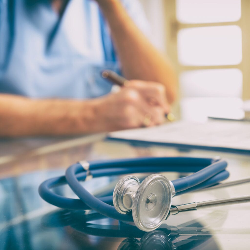 A nurse practitioner writing as a stethoscope is in the foreground