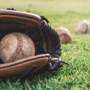 A baseball glove with a baseball inside on the grass, with two baseballs in the background